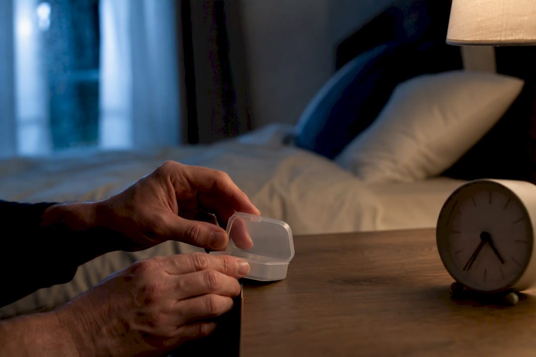 Handen die een pillendoosje openen naast het nachtkastje met klok